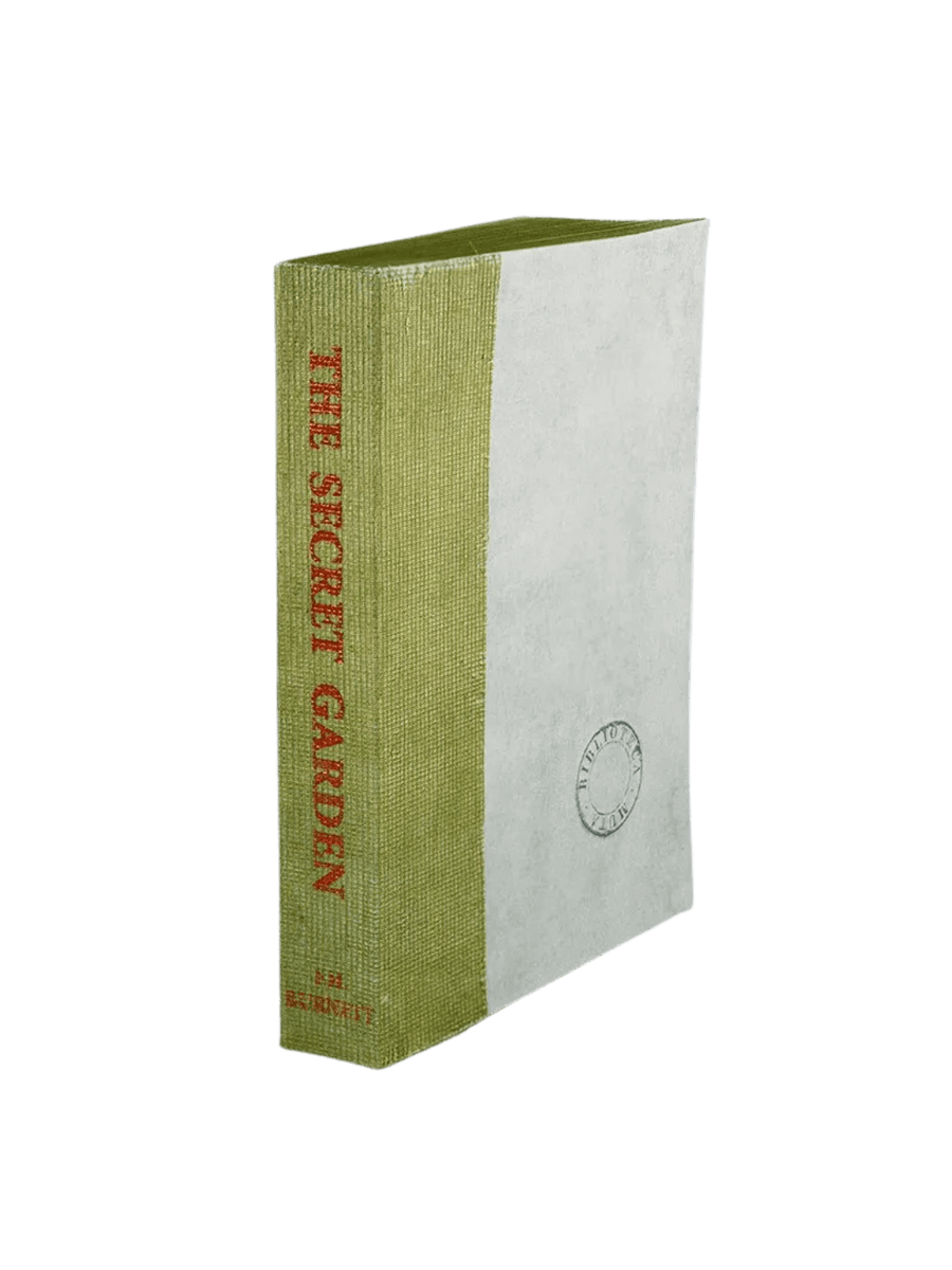 A Biblioteca Muta: The Secret Garden journal from Slow Design featuring a light green gauze spine stamped with a red literary title alongside a textured, parchment-like cover bearing a circular library seal | Twentyseven Toronto