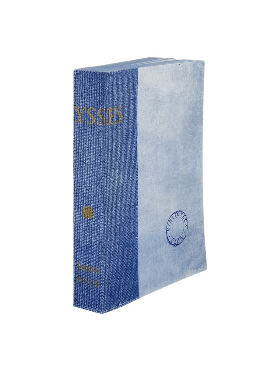 A notebook from the Biblioteca Muta: Ulysses from Slow Design collection features a textured blue gauze spine stamped with gold literary typography alongside a light blue parchment-style cover bearing a circular library seal | Twentyseven Toronto