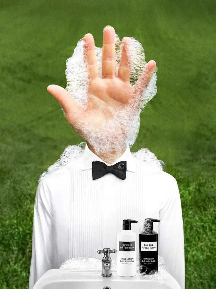 Person in formal attire with soapy hands and bottles on a grass background using DS&Durga 'Big Sur After Rain' hand soap and hand lotion | Twentyseven Toronto