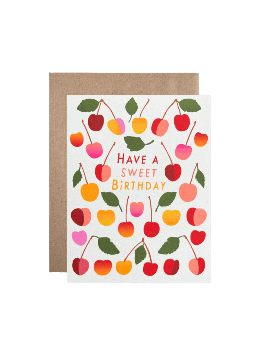 The Hartland Cards Birthday Sweet Cherries Card features a white background covered in colorful illustrated red, pink, orange, and yellow cherries with green leaves, framing the text "Have a Sweet Birthday" in red, pink, and yellow lettering, paired with a brown kraft envelop | Twentyseven