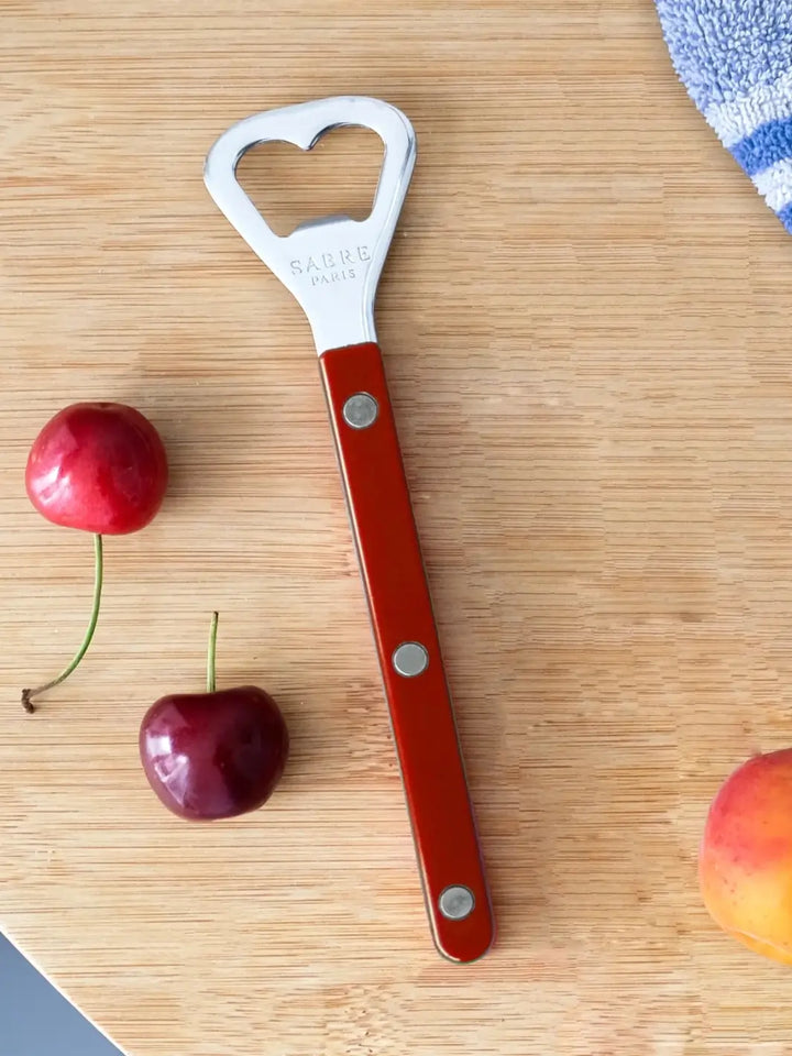 Sabre Paris Shiny Bistrot Solid Bottle Opener in Burgundy shot on a light wood cutting board, surrounded by fresh cherries and a peach | Twentyseven Toronto