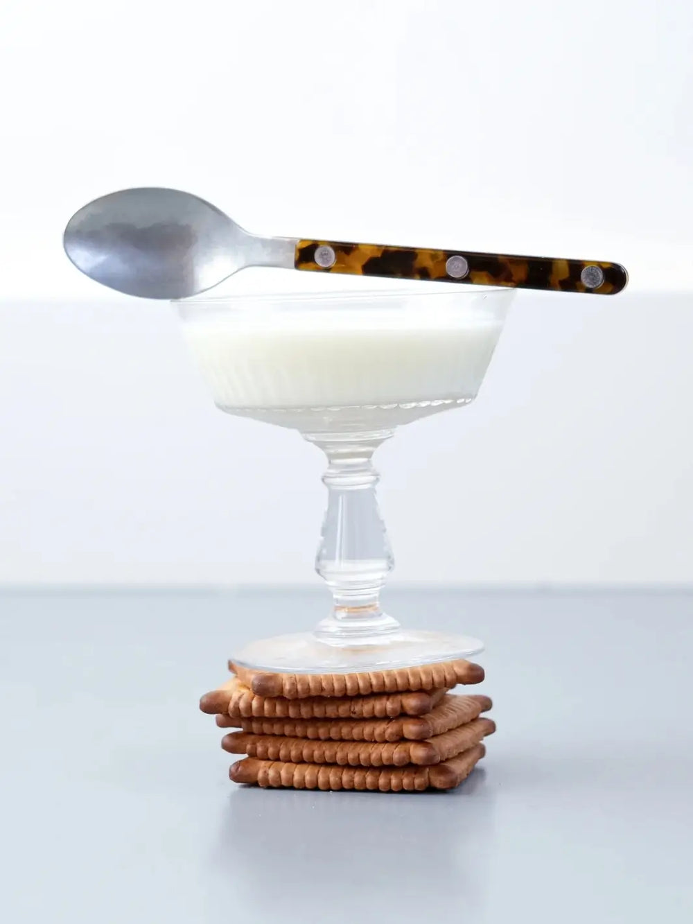 A teaspoon from the Sabre Paris Bistrot Solid Shiny 5 Piece Cutlery Set in Faux Tortoise atop the rim of a glass coupe filled with a white creamy liquid | Twentyseven Toronto