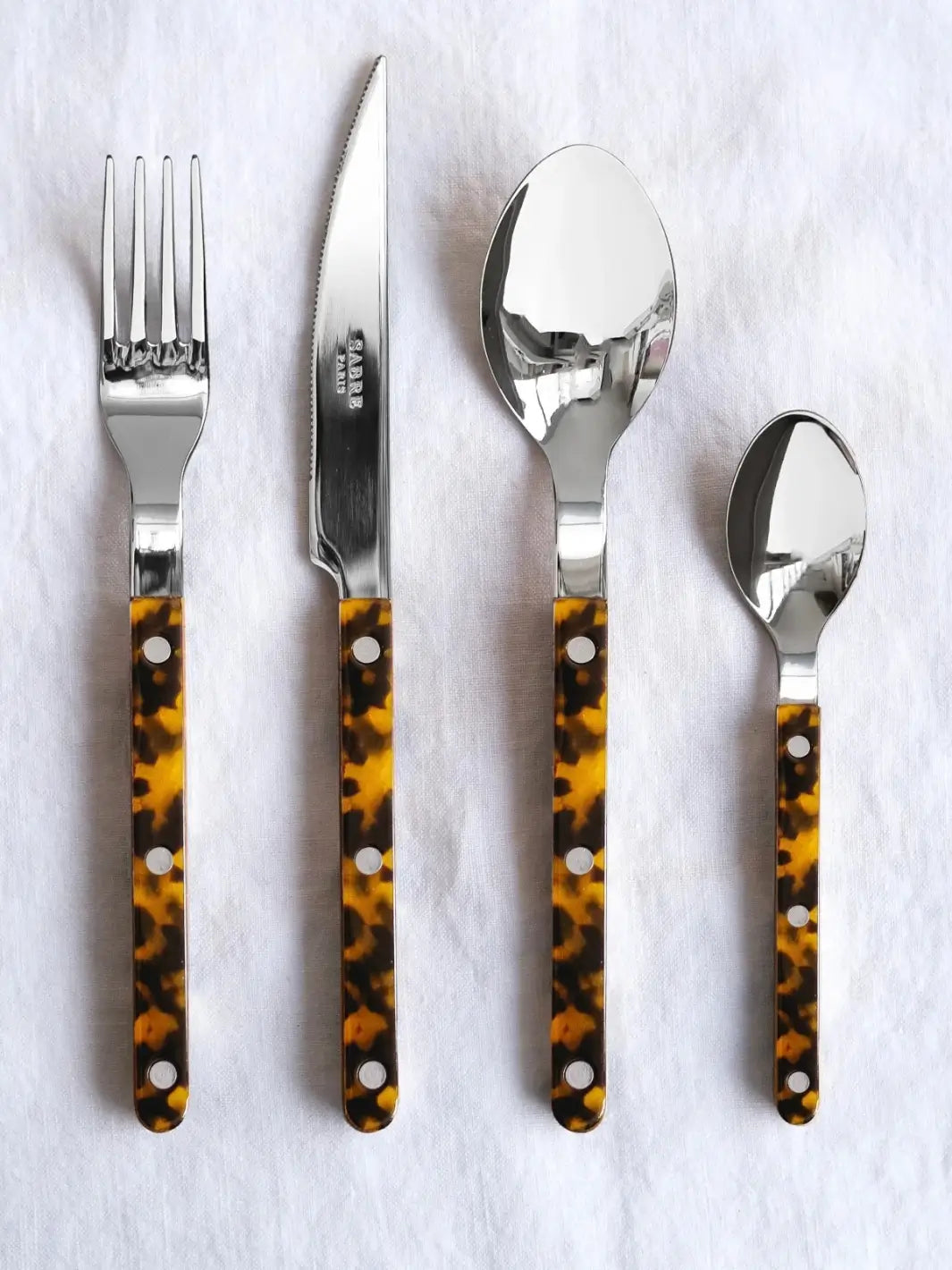 Four pieces from the Sabre Paris Bistrot Solid Shiny 5 Piece Cutlery Set in Faux Tortoise, including a soup spoon, a dinner fork, a dinner knife and a teaspoon | Twentyseven Toronto