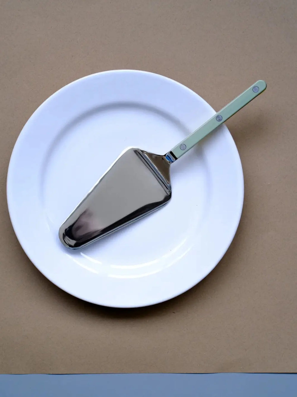 Sabre Paris Bistrot Solid Shiny Tart Server in Asparagus resting diagonally across a clean white ceramic plate against a brown background | Twentyseven Toronto