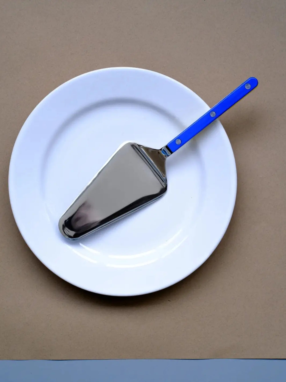 Sabre Paris Bistrot Solid Shiny Tart Server in Lapis Blue resting diagonally across a clean white ceramic plate against a brown background | Twentyseven Toronto