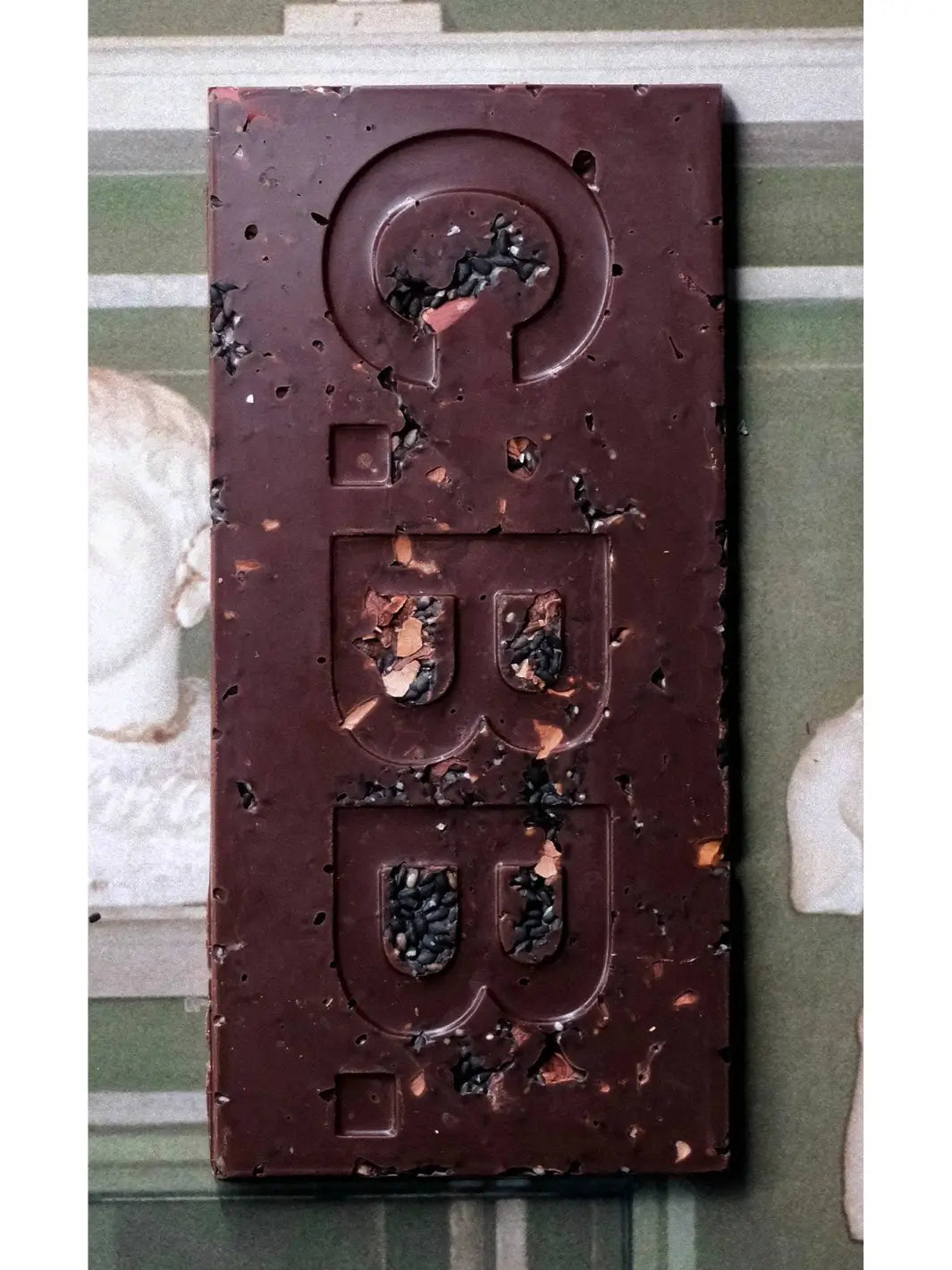 A close-up view of the Black Toasted Sesame Seeds, Cacao Shell & Nibs Chocolate Bar from Casa Bosques reveals the intricate logo molding and textured inclusions of seeds and cacao nibs | Twentyseven Toronto