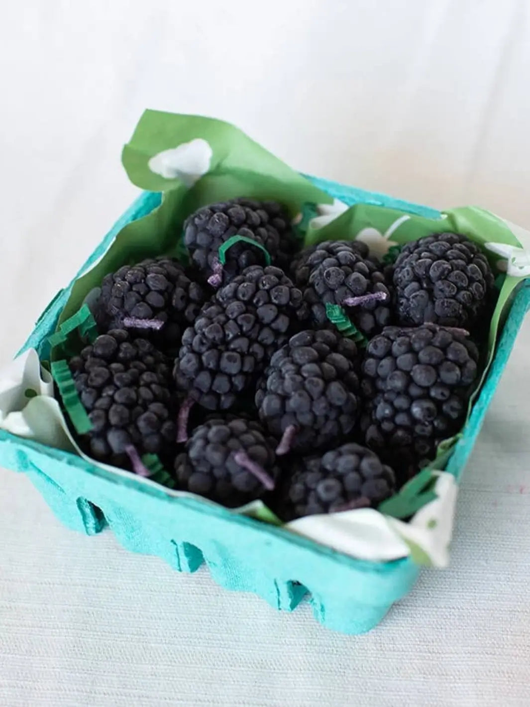 Blackberry-shaped beeswax candles from Happy Organics in a blue container on a white background | Twentyseven Toronto