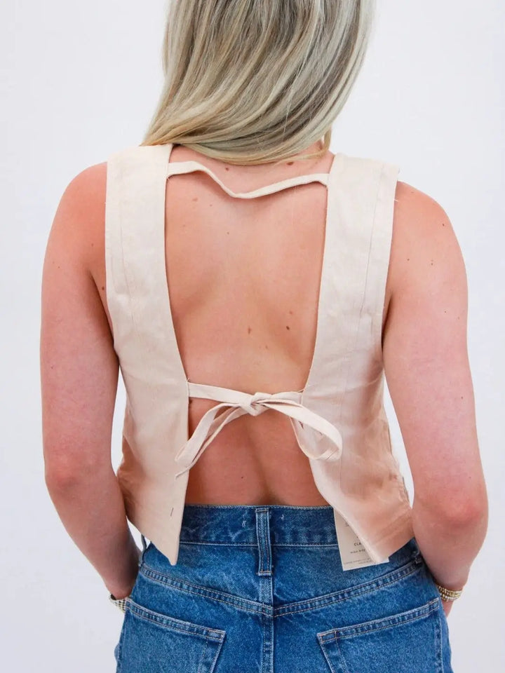 A view from behind highlights the dramatic open-back design and delicate self-tie bow closure of the cream-colored Free People We The Free Blake Vest - Sand Dollar | Twentyseven Toronto