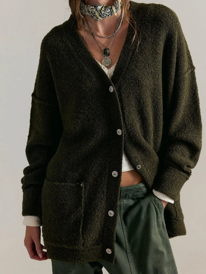 A front view shows the longline Free People Blazing Cardi in Dark Green partially buttoned and styled with silver layered necklaces, a patterned neck scarf, and green pants | Twentyseven Toronto