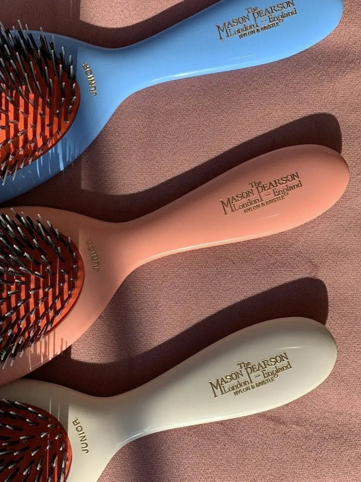 A close-up shot highlights the gold lettering stamped onto the handles of the blue, pink, and white variations of the Mason Pearson Boar Bristle & Nylon Mix Hair Brush | Twentyseven Toronto