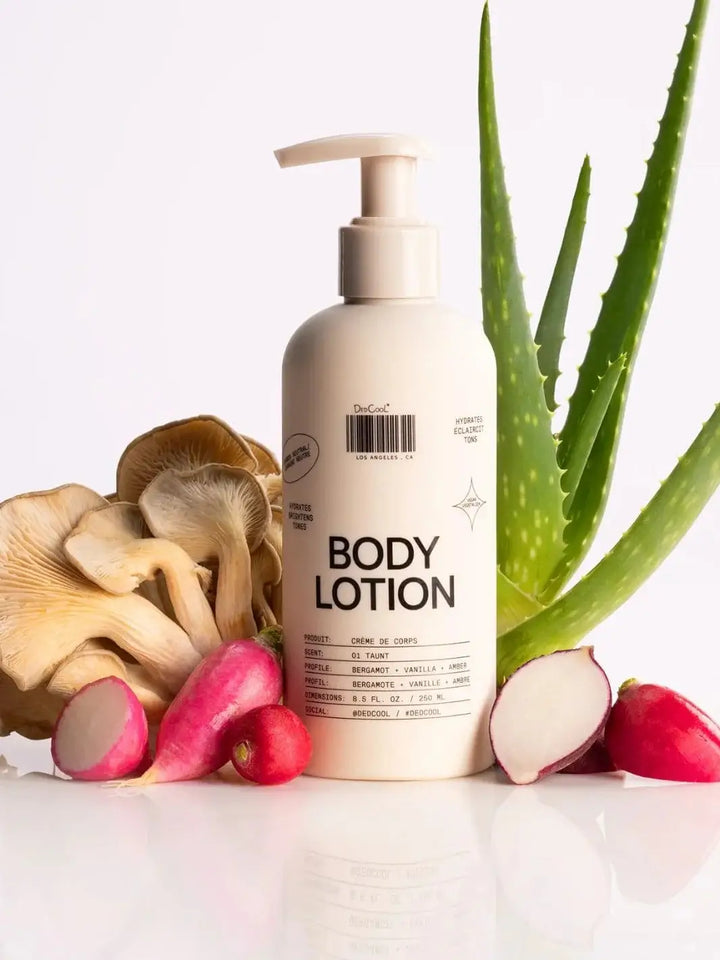 A white pump bottle of Dedcool Body Lotion 01 "Taunt" on a clean white surface alongside fresh oyster mushrooms, radishes, and an aloe vera plan | Twentyseven Toronto