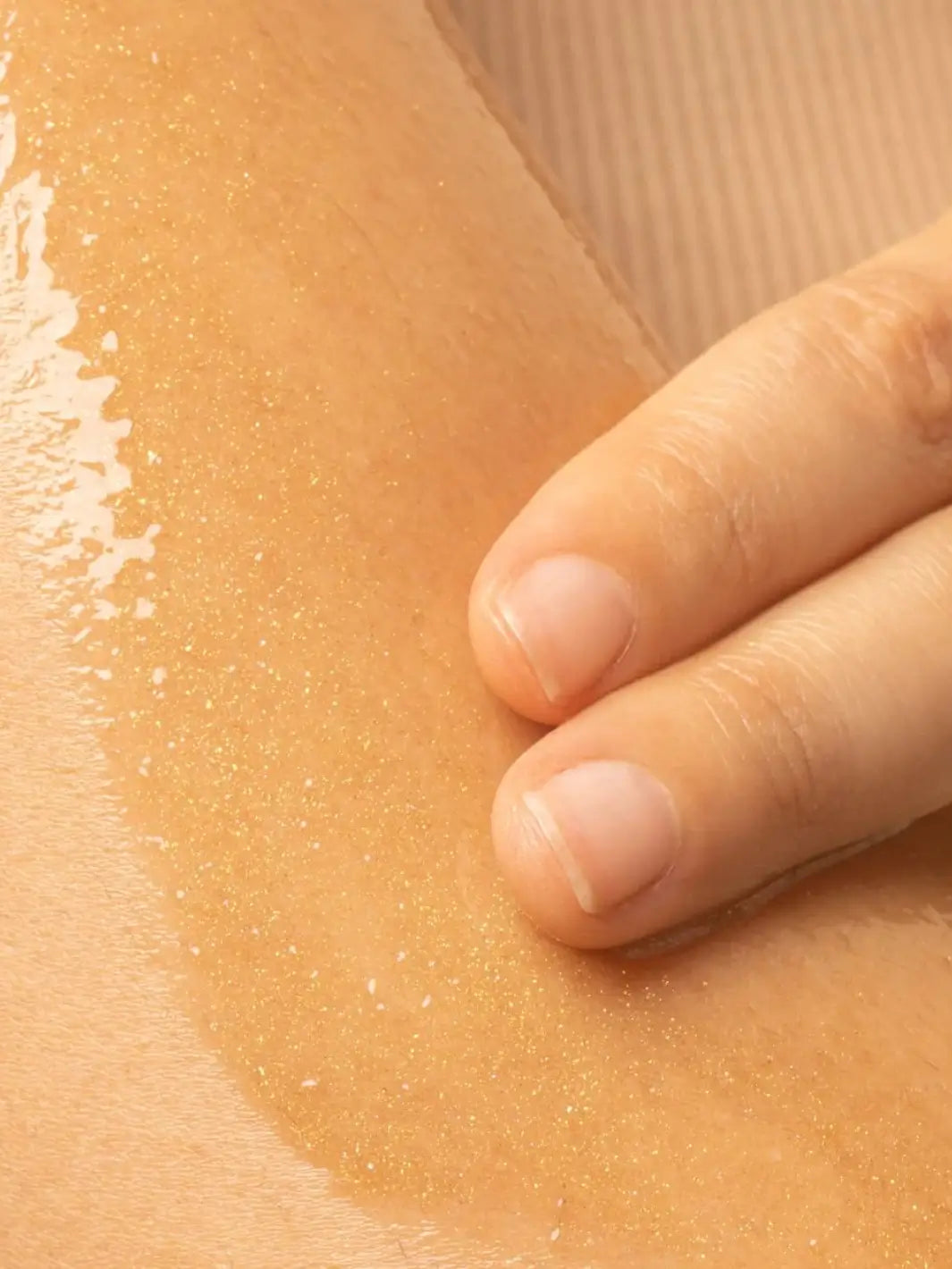 A close-up shot shows two fingers rubbing a thin layer of the shimmering Beauty from Bees Body Serum - Summer Glow onto a person's skin | Twentyseven Toronto