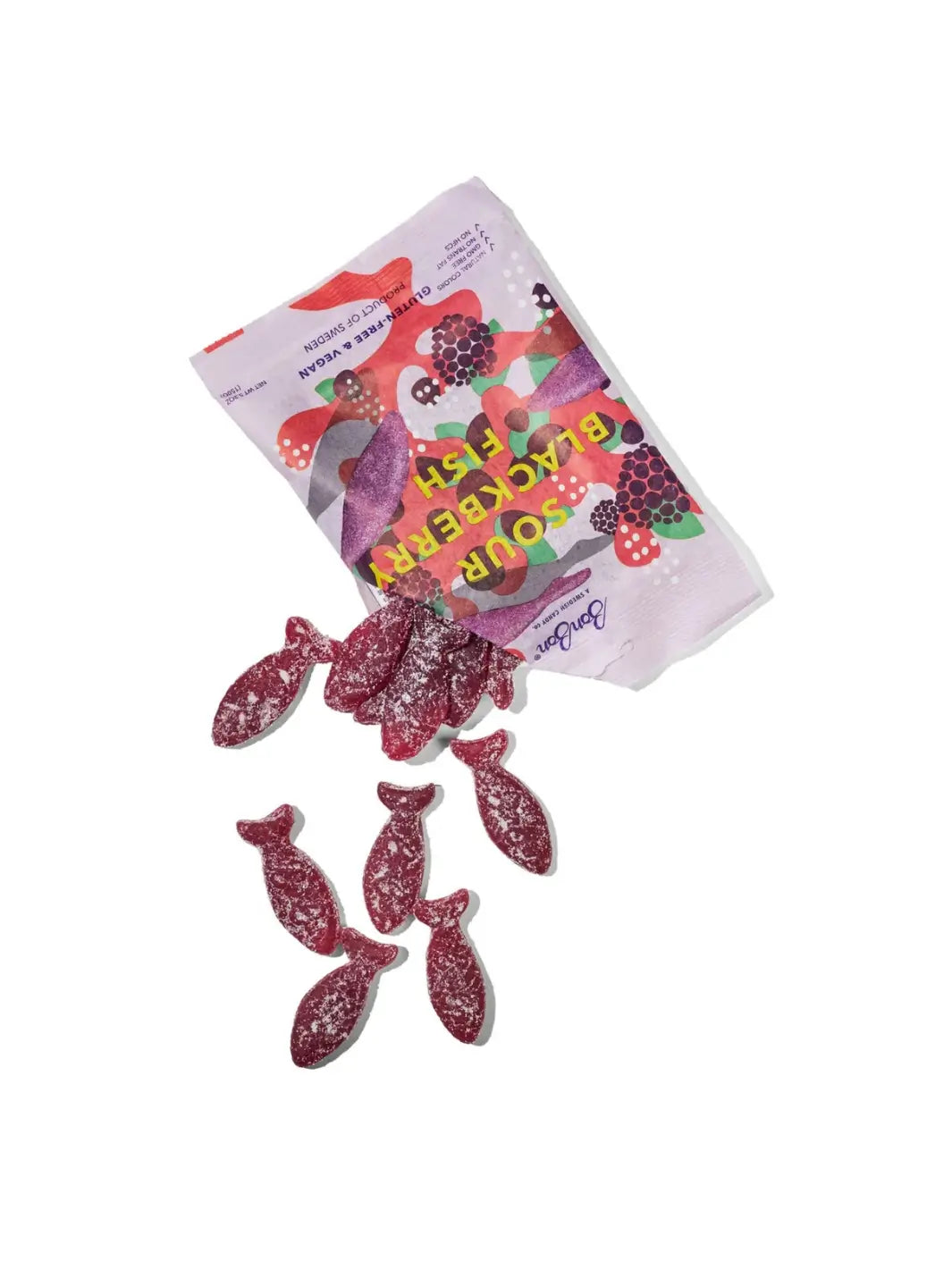 A bag of BonBon Swedish Candy Sour Blackberry Fish gummies lies on its side with several fish-shaped gummies spilled out onto a clean white background. The packaging features colorful illustrations of blackberries | Twentyseven Toronto