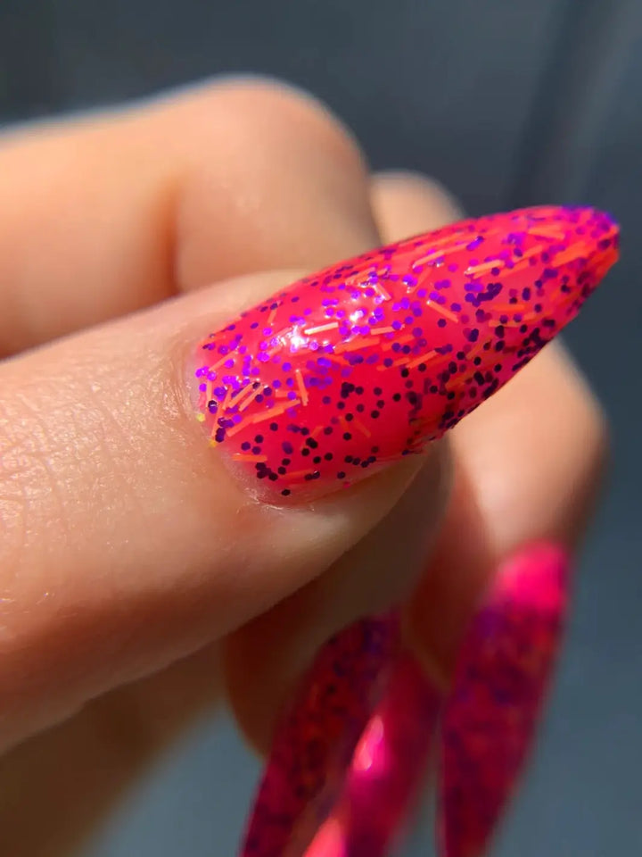 Close up on a single stiletto fingernail coated in Death Valley Nails Bone Daddy Nail Polish, highlighting the orange bar shreds embedded in the neon pink formula | Twentyseven Toronto
