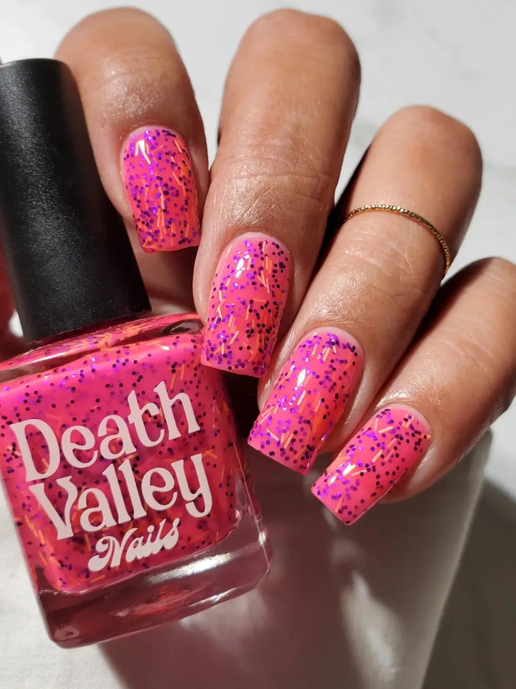 A hand with long, square-shaped fingernails wearing bright pink Death Valley Nails Bone Daddy Nail Polish holding its glass bottle | Twentyseven Toronto