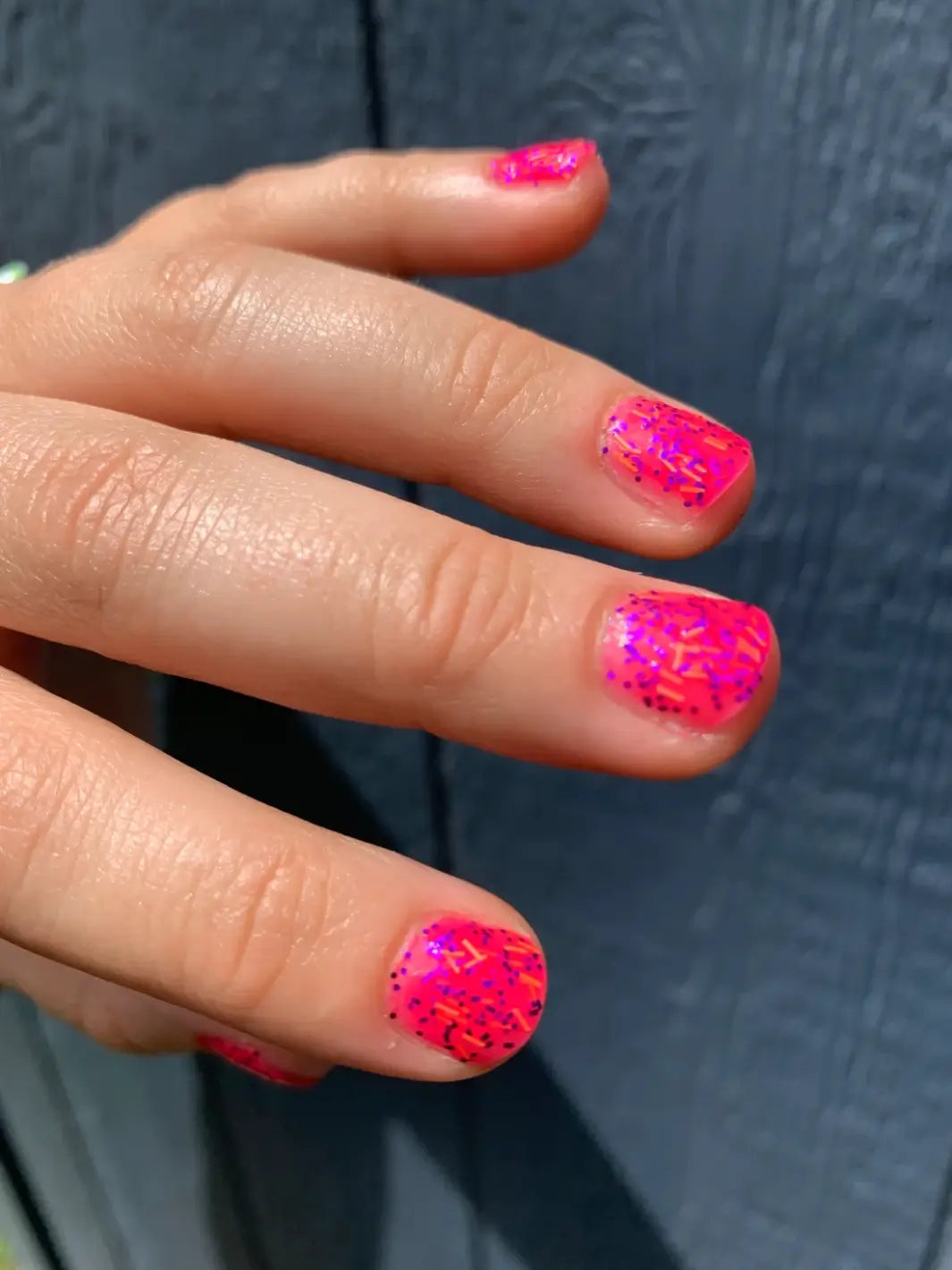 A close-up shot under direct light shows short, rounded fingernails painted with a bright pink Death Valley Nails Bone Daddy Nail Polish against a dark textured background | Twentyseven Toronto