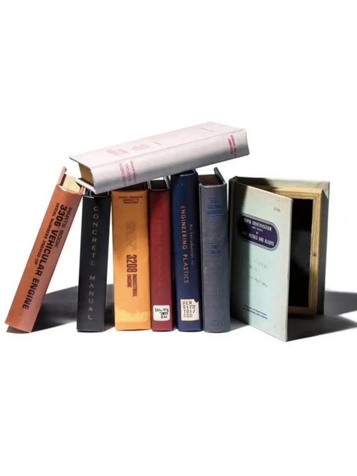A variety of vintage-style textbook designs are stacked and stood upright together to showcase the full hidden storage options within the Book Storage Box Collection from Puebco | Twentyseven Toronto