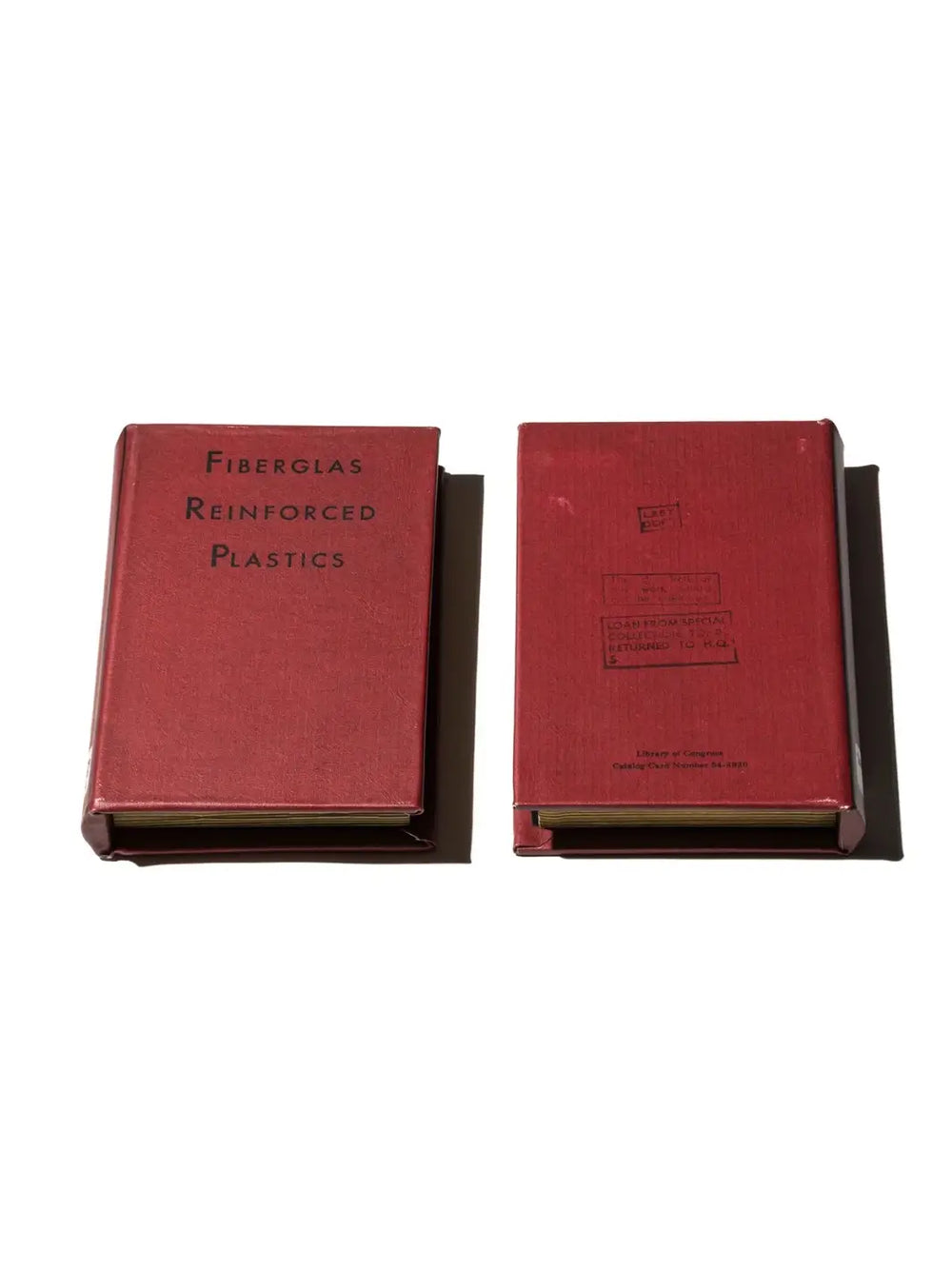 Two red vintage-style Book Box - Fiberglass Plastics from Puebco organizers are shown lying flat, displaying the front cover text on one and the stamped library details on the back cover of the other | Twentyseven Toronto