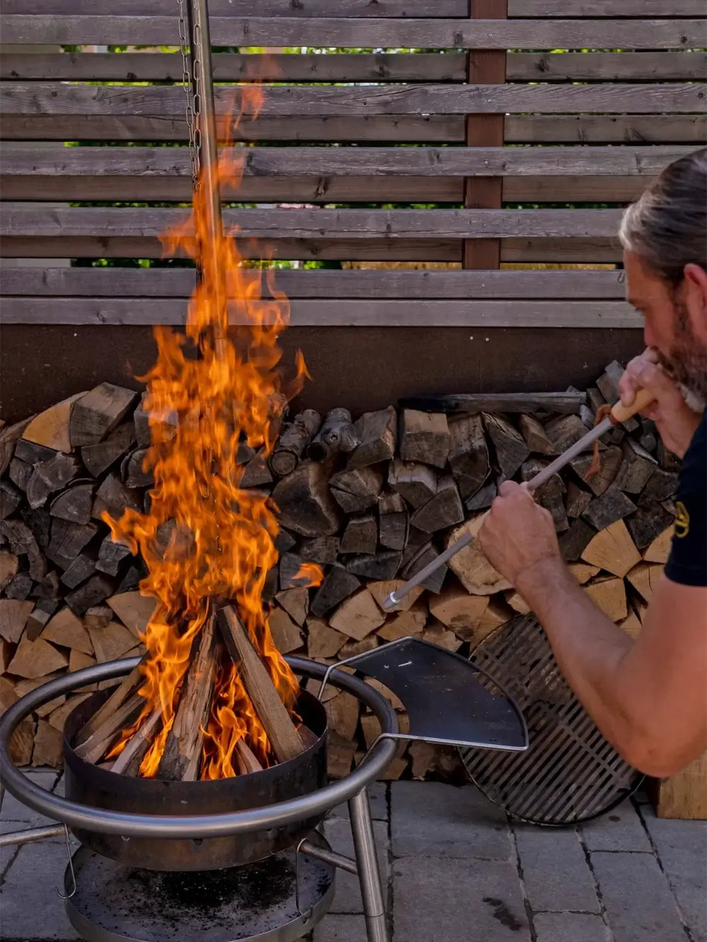 Person using a Bouffadou-Flame Blower tool from Burstenhaus Redecker to tend to a fire pit filled with wood | Twentyseven Toronto