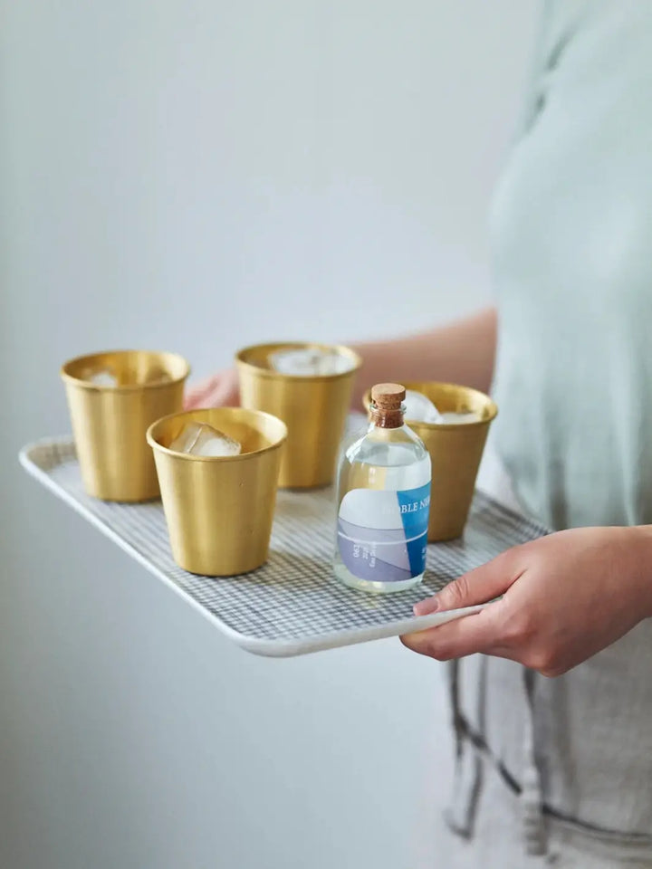 A person holds a tray carrying a small glass bottle and four ice-filled Fog Linen Work Brass Cups ready for serving drinks | Twentyseven Toronto