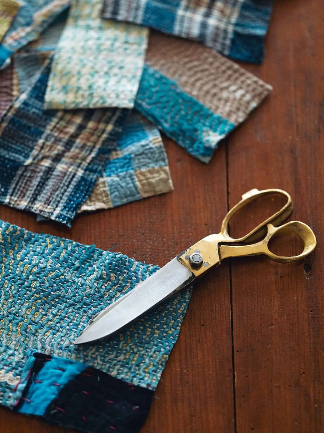 A pair of Brass Handle Scissors Large from Fog Linen Work rests on a rustic wooden table alongside a stack of linen fabric and a measuring tape | Twentyseven Toronto