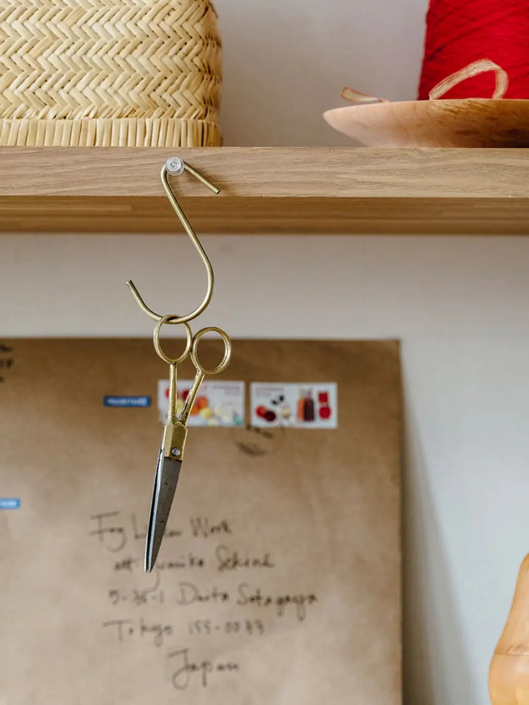 An S-hook hanging from a wooden shelf holds the Brass Handle Scissors Small from Fog Linen Work in a bright, organized craft room | Twentyseven Toronto