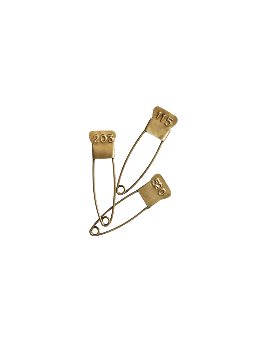 A set of three vintage-inspired Brass Number Pin from Fog Linen Work fasteners, displaying different three-digit codes on their antique-style heads | Twentyseven Toronto