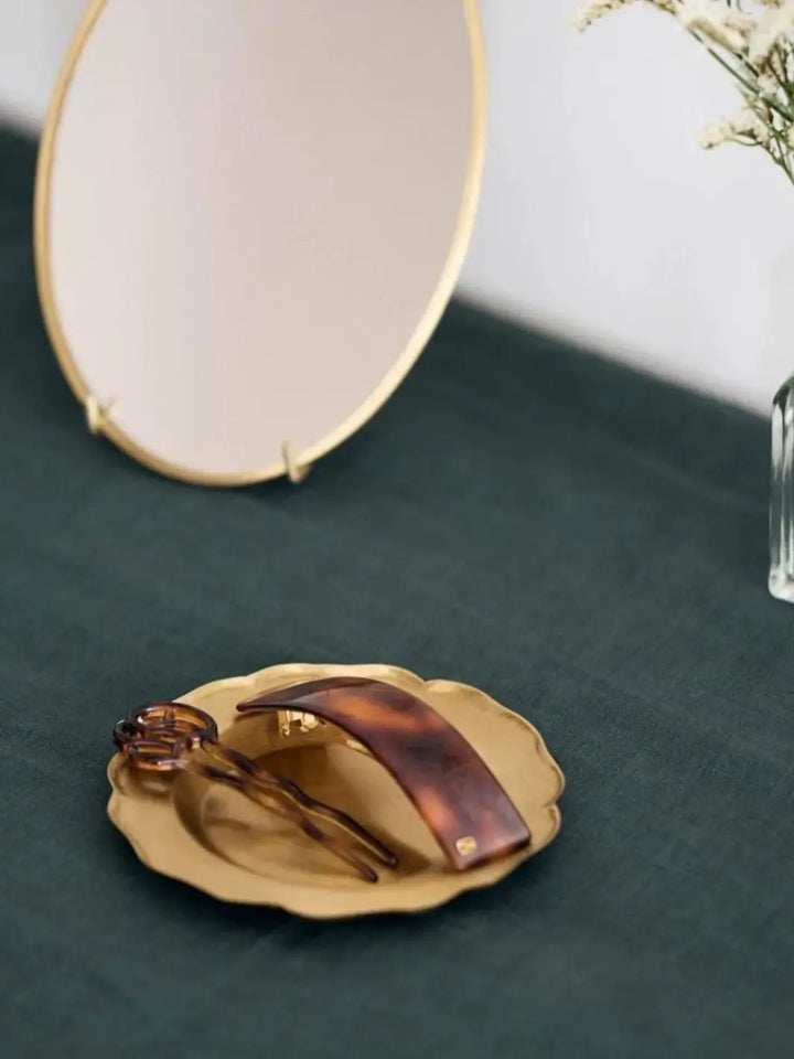 Fog Linen Work Brass Ruffle Edge Tray Small sits on a dark green linen tablecloth, serving as a jewelry dish for a tortoiseshell hair clip and pin | Twentyseven Toronto