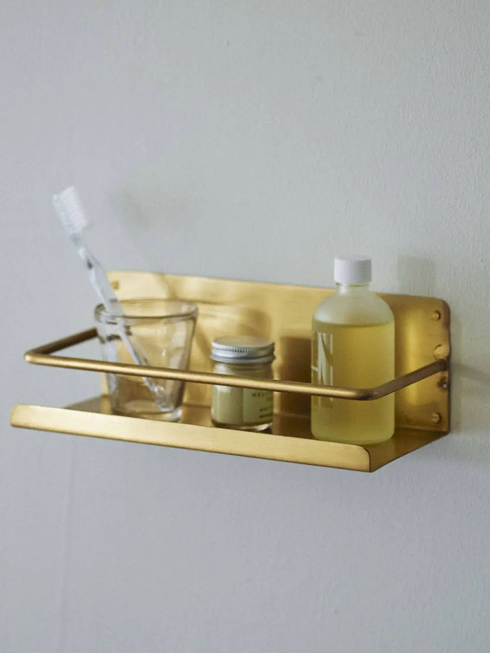 In a bathroom setting, the Brass Shelf from Fog Linen Work provides a functional storage solution for a toothbrush and various apothecary bottles | Twentyseven Toronto