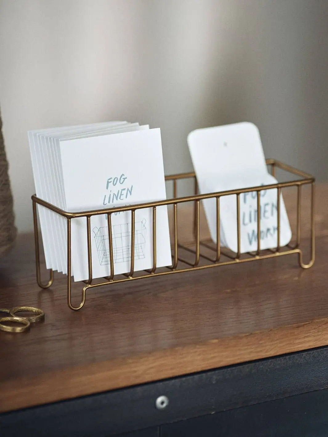 Stacks of branded white note cards neatly organized inside a Fog Linen Work Brass Wire Basket Narrow on a dark wooden tabletop | Twentyseven Toronto