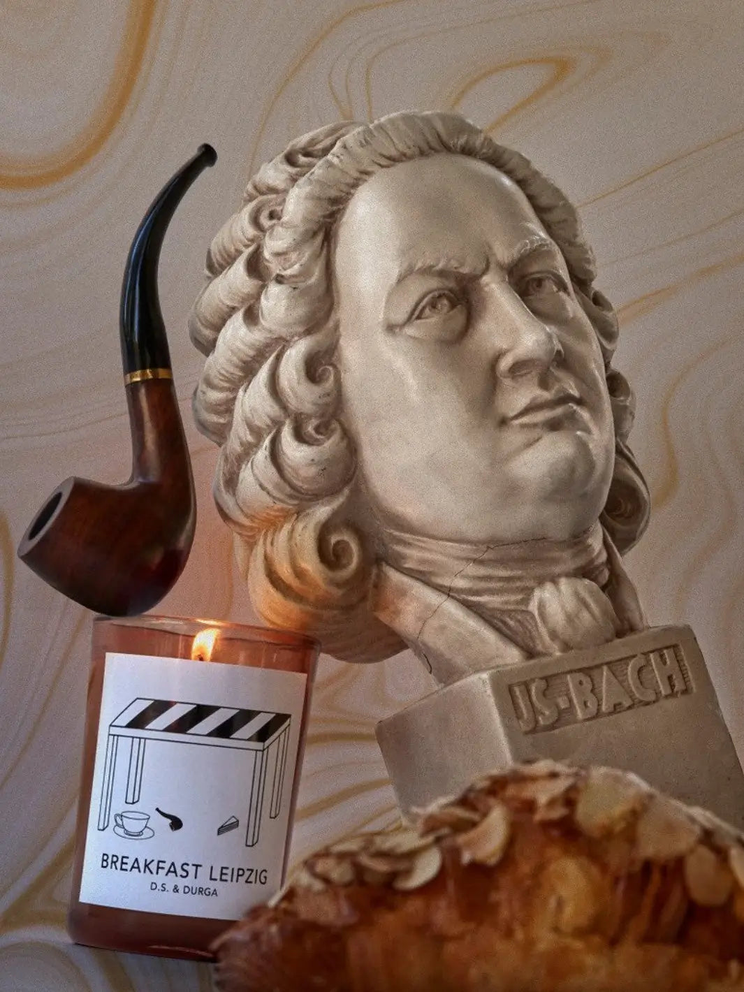 Candle labeled 'Breakfast Leipzig' from DS&Durga with a pipe and pastry in front of a bust of JS Bach | Twentyseven Toronto