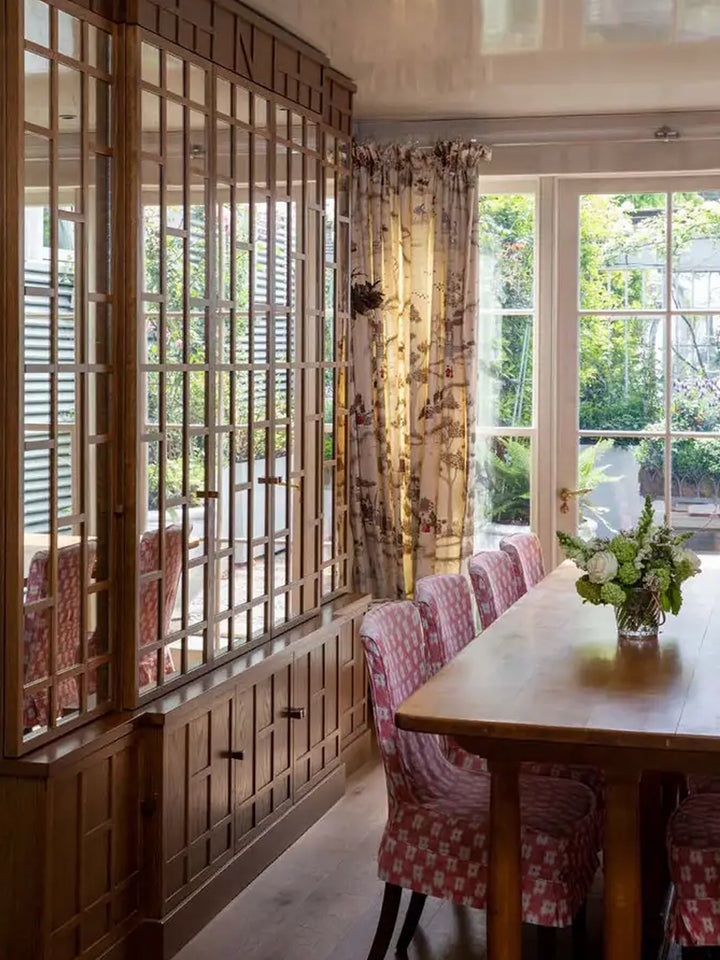Dining room featured in British Designers at Home, with wood cabinetry, patterned dining chairs and floral curtains | Twentyseven Toronto