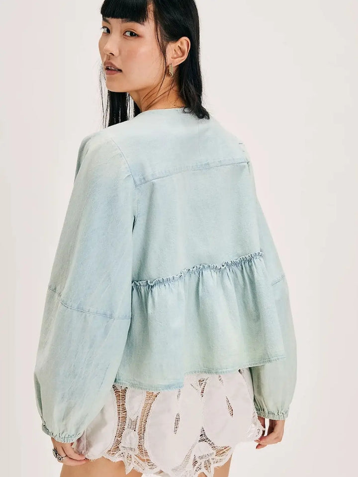 A view from behind shows a model wearing the light-wash Free People Brunch Babe Denim Blouse featuring a ruffled peplum waist seam and voluminous long sleeves | Twentyseven Toronto