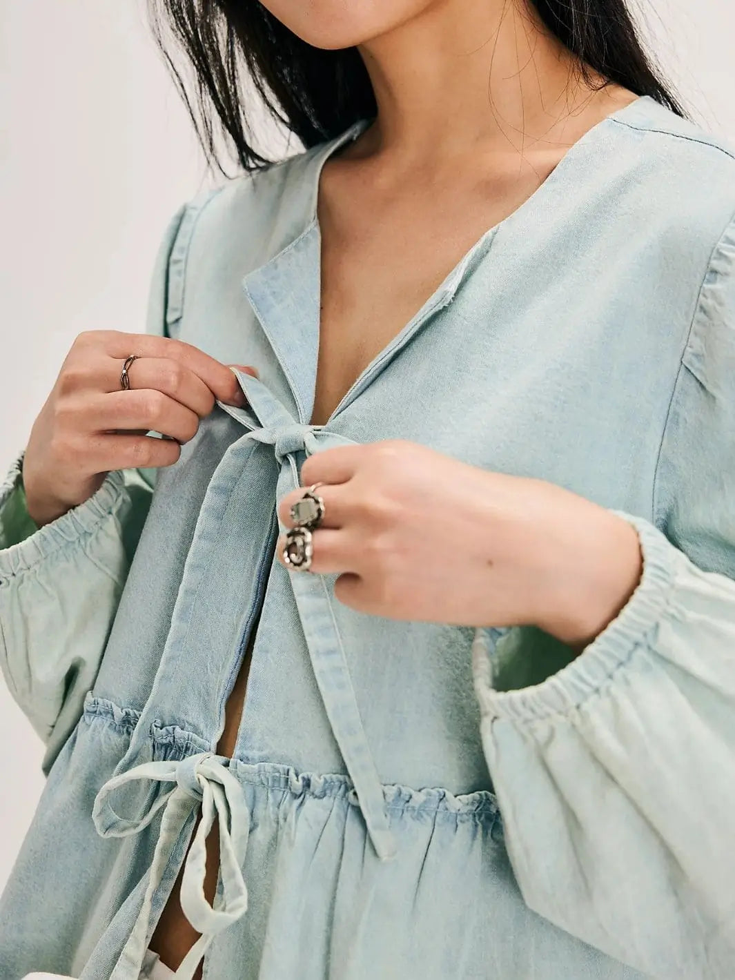 A close-up shot focuses on the front tie closures, V-neckline, and elastic cuffs of the Free People Brunch Babe Denim Blouse | Twentyseven Toronto