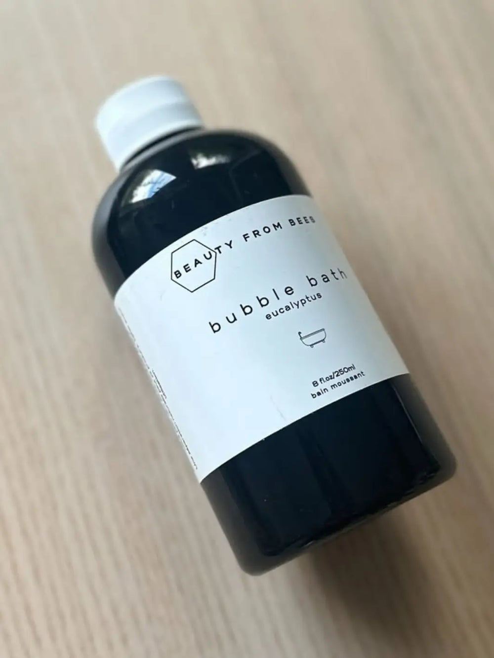 Bottle of bubble bath in Eucalyptus labeled 'Beauty from the Bees' on a wooden surface | Twentyseven Toronto
