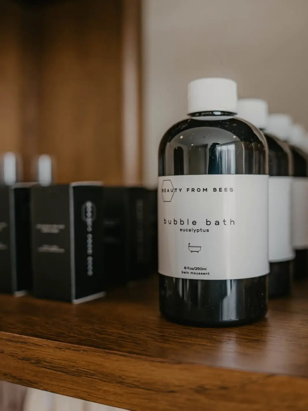Bottle of bubble bath in Eucalyptus with a 'Beauty from Bees' label on a wooden surface, surrounded by more bottles | Twentyseven Toronto