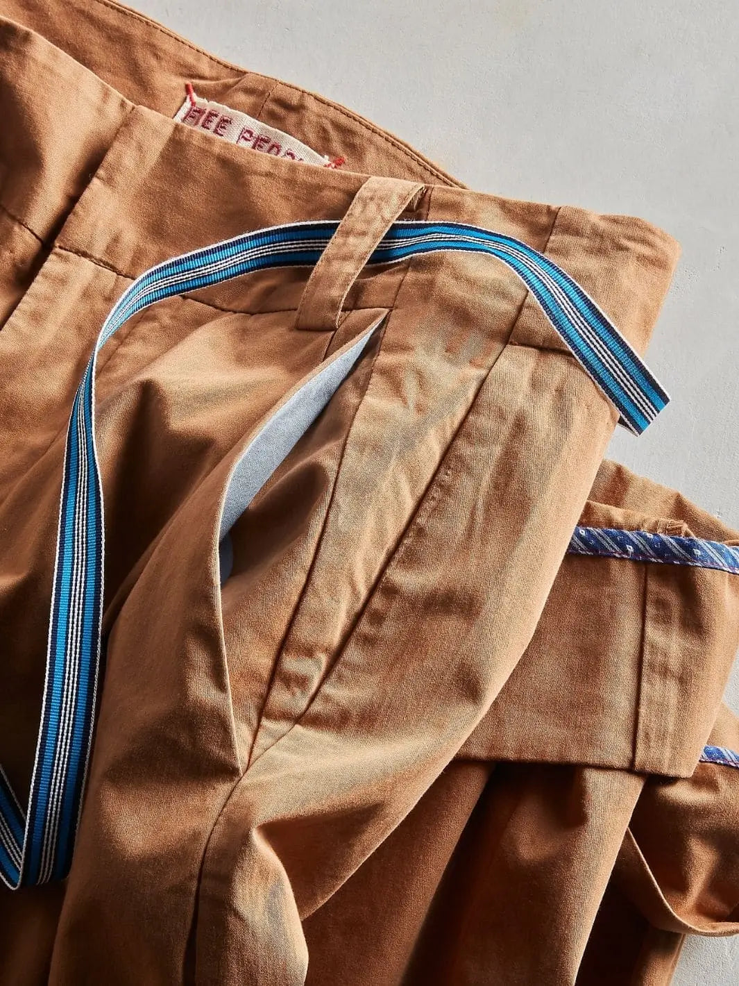 A close-up top-down view highlights the fabric texture, belt loops, and side pocket placement of the Free People Buckle Back Trousers - Tobacco Combo | Twentyseven Toronto