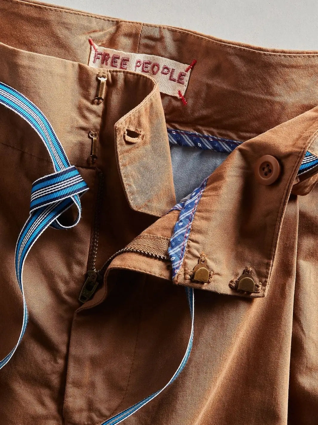 An open detail shot focuses on the interior lining pattern, zipper fly, and metal clasp closures of the Free People Buckle Back Trousers - Tobacco Combo | Twentyseven Toronto
