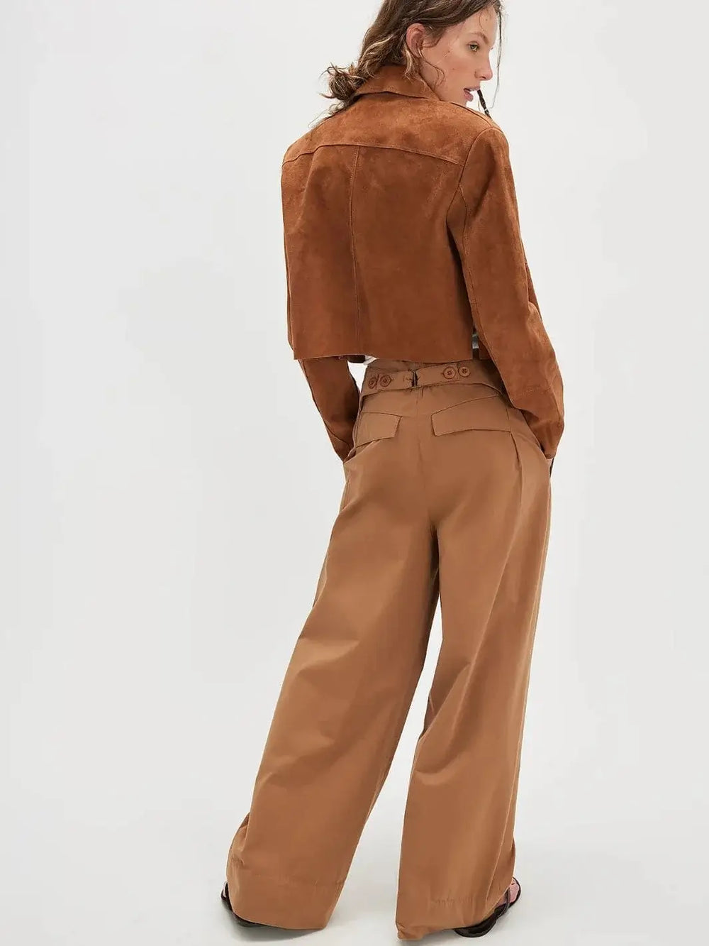 A rear view captures a model wearing the mid-rise Free People Buckle Back Trousers - Tobacco Combo paired with a cropped brown suede jacket | Twentyseven Toronto