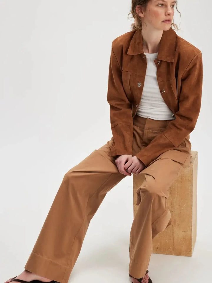 A model sits on a wooden block showcasing the loose, straight-leg silhouette of the Free People Buckle Back Trousers - Tobacco Combo | Twentyseven Toronto