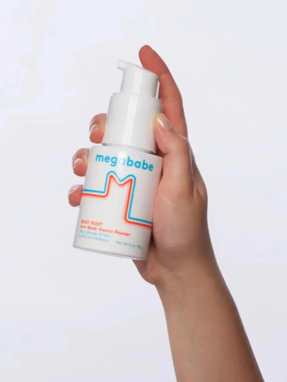 A hand holds up a white pump bottle of Megababe Bust Dust against a clean white background to showcase the product's packaging | Twentyseven Toronto