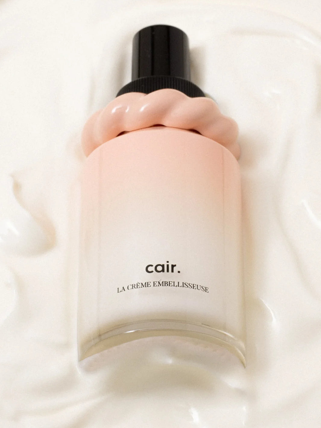 Cair Leave-In Hair Cream bottle resting in a soft white cream texture, featuring its blush pink bottle and sculptural cap | Twentyseven Toronto