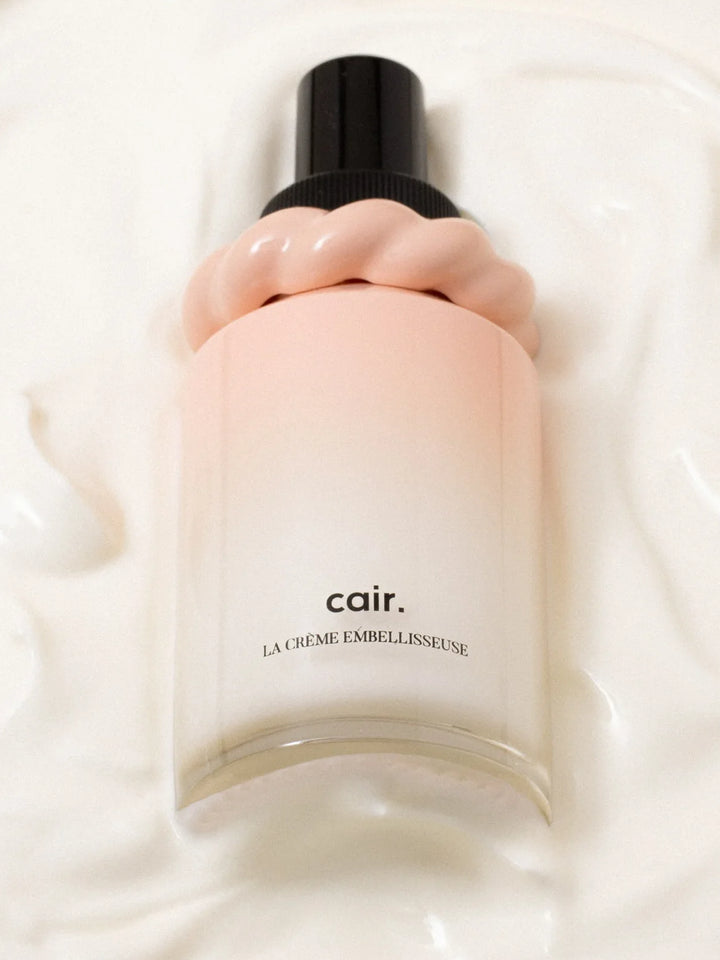 Cair Leave-In Hair Cream bottle resting in a soft white cream texture, featuring its blush pink bottle and sculptural cap | Twentyseven Toronto