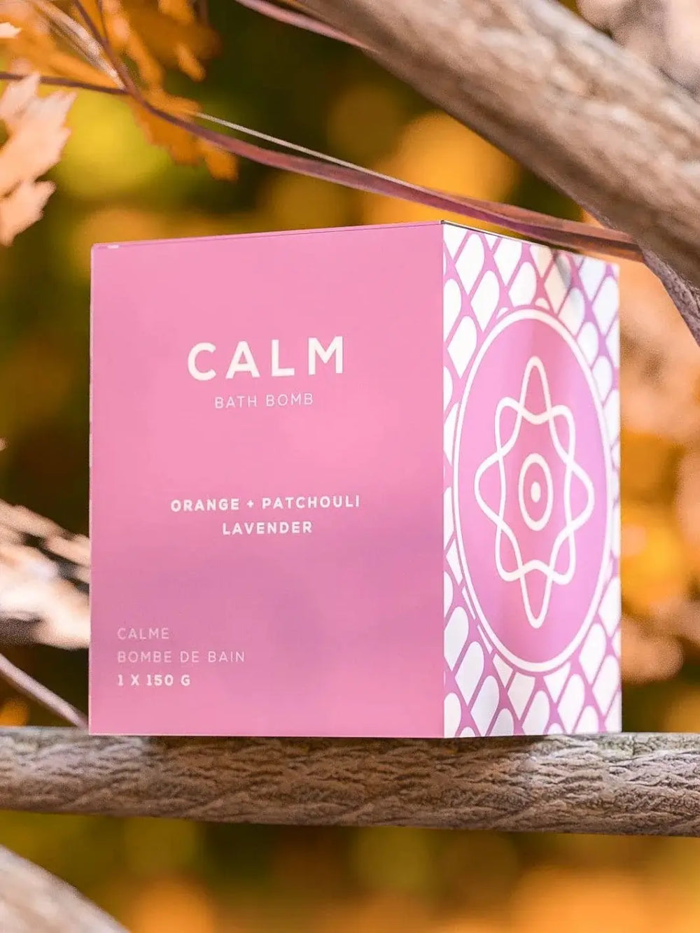 The pink packaging of the Bare Skin Bar CALM Bath Bomb sits outdoors between tree branches against a soft, sunlit autumn background | Twentyseven Toronto