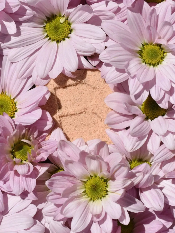 A flat lay view shows a peach-colored the unwrapped Bare Skin Bar CALM Bath Bomb surrounded by light pink daisy flowers | Twentyseven Toronto