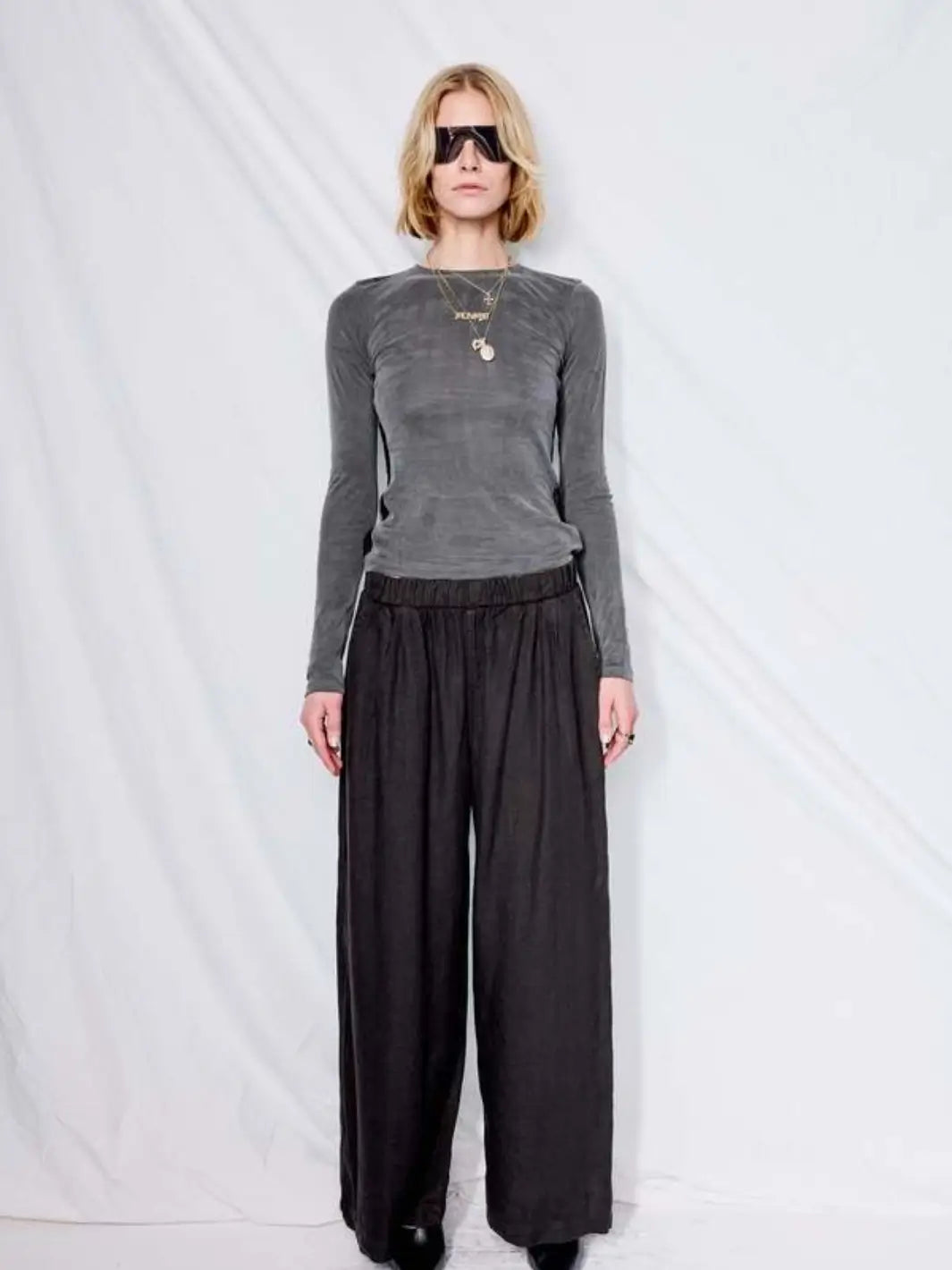A model poses in front of a white backdrop wearing a grey long-sleeve top styled with the wide-leg, relaxed-fit Jungmaven Cambria Pant - Black | Twentyseven Toronto