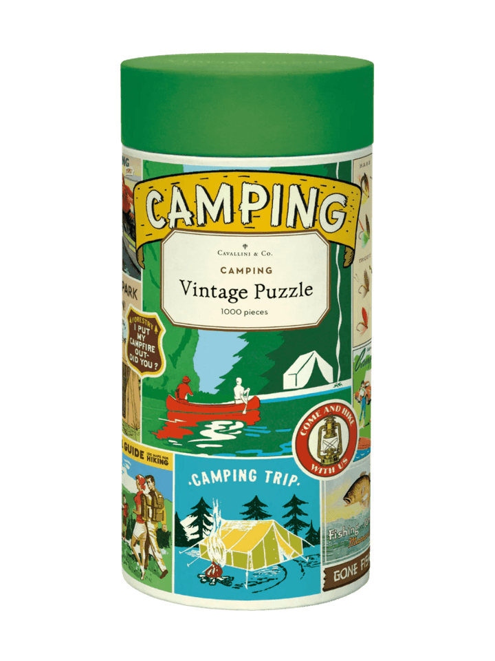 Cylindrical paper tube for the Cavallini Paper & Co Camping 1000 Piece Puzzle with a green cap, highlighting a central title card above an illustration of a red canoe on a river | Twentyseven Toronto