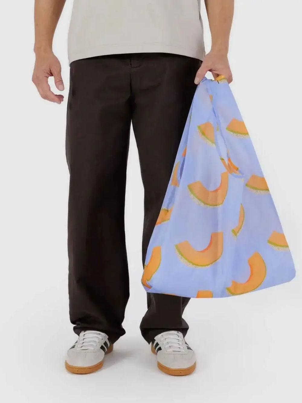 A person standing against a plain white background holds a light blue reusable bag printed with orange cantaloupe slices, showcasing the Baggu Cantaloupe Blue Bag | Twentyseven Toronto