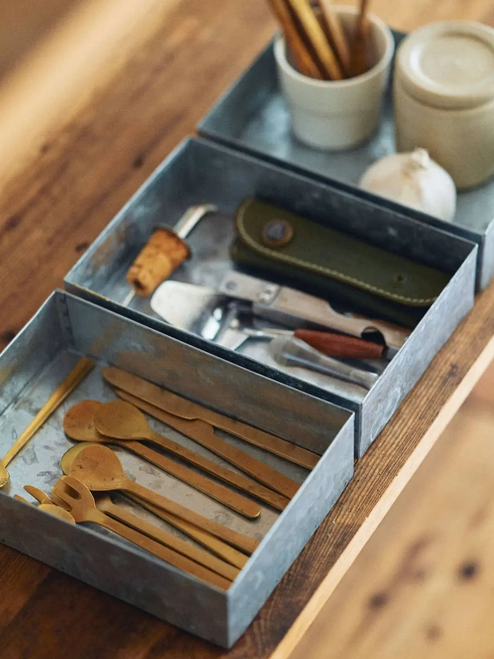 Three Fog Linen Work Card Box trays are arranged on a wooden surface, neatly organizing brass cutlery, wine tools, and kitchen accessories | Twentyseven Toronto