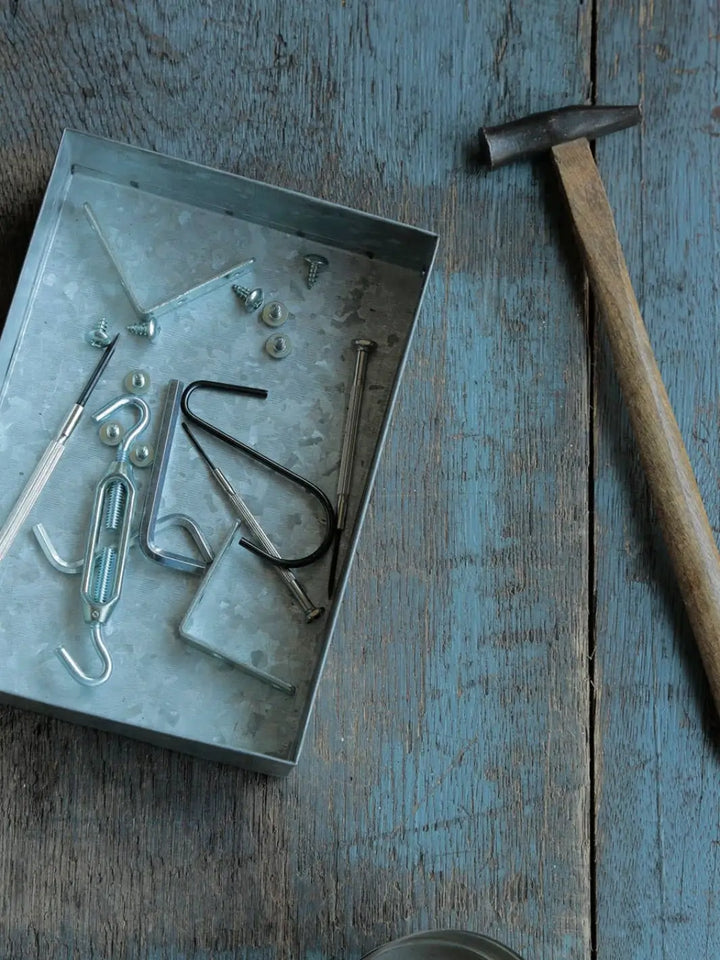 A Fog Linen Work Card Box sits on a rustic blue wooden workbench, holding an assortment of metal hardware, screws, and hooks next to a hammer | Twentyseven Toronto